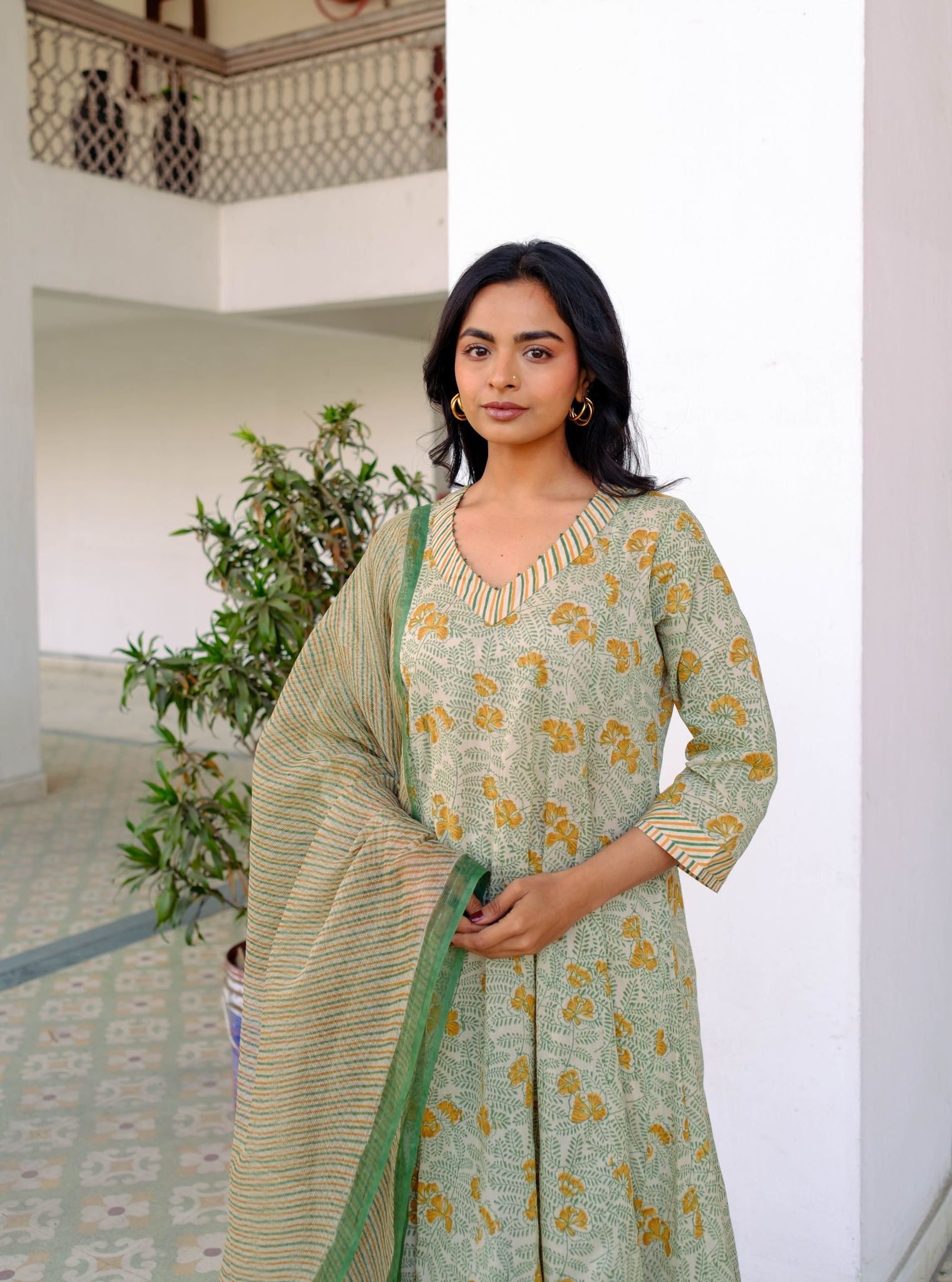 Woman wearing a green and yellow patterned outfit with a plant in the background