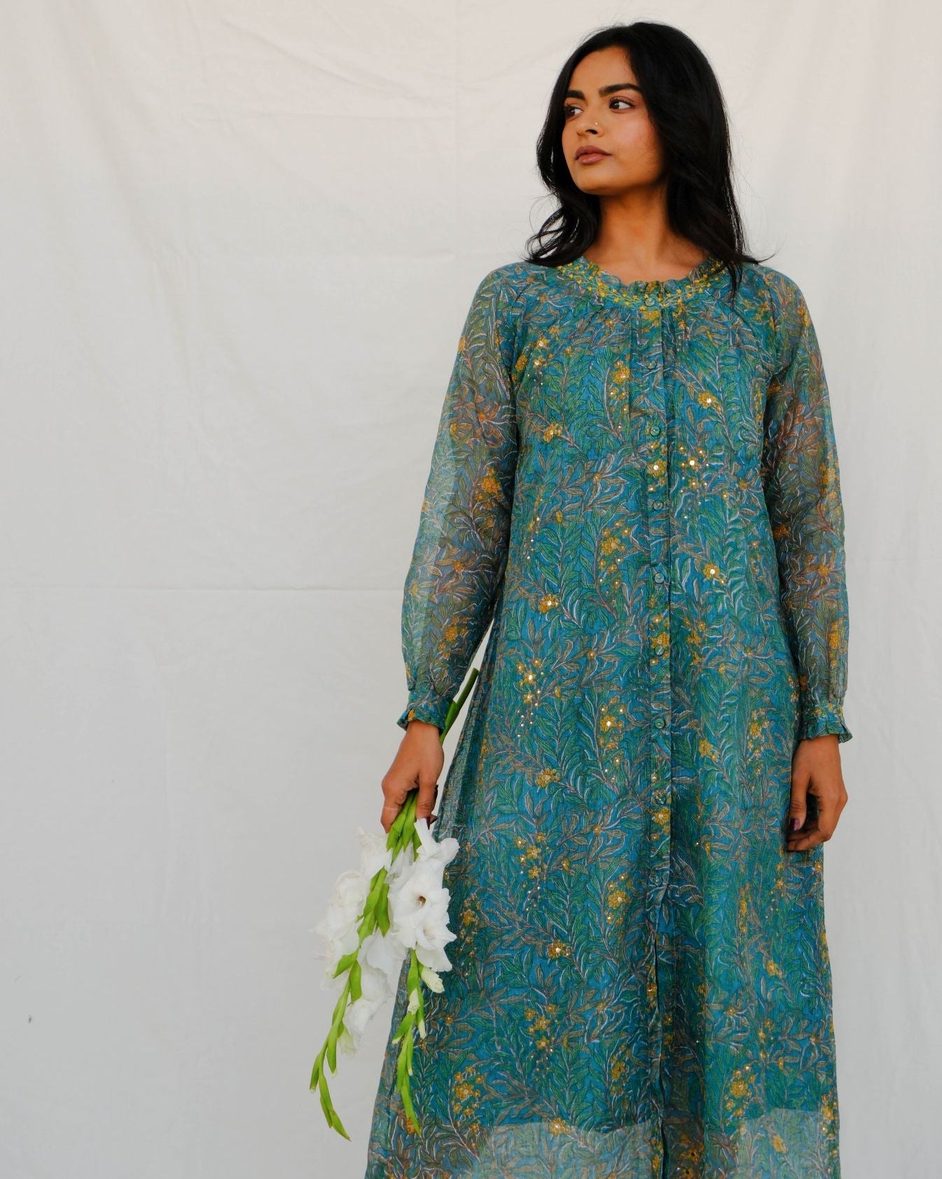 Woman wearing a teal patterned dress holding white flowers against a white background
