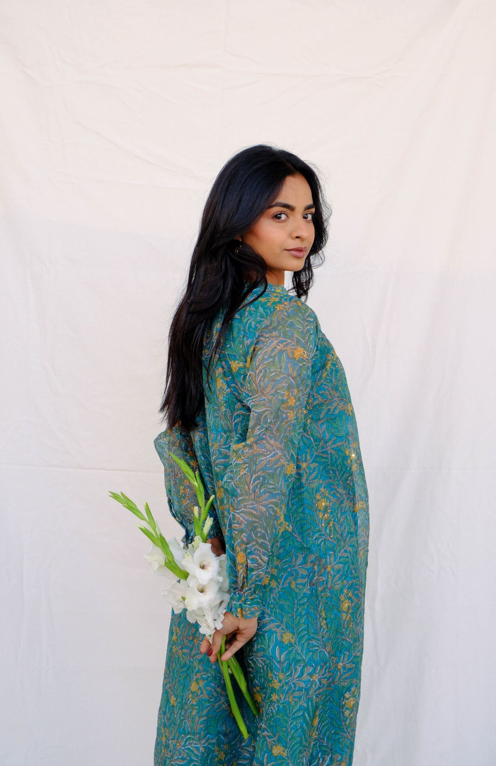 Woman in a teal patterned outfit holding white flowers against a white background