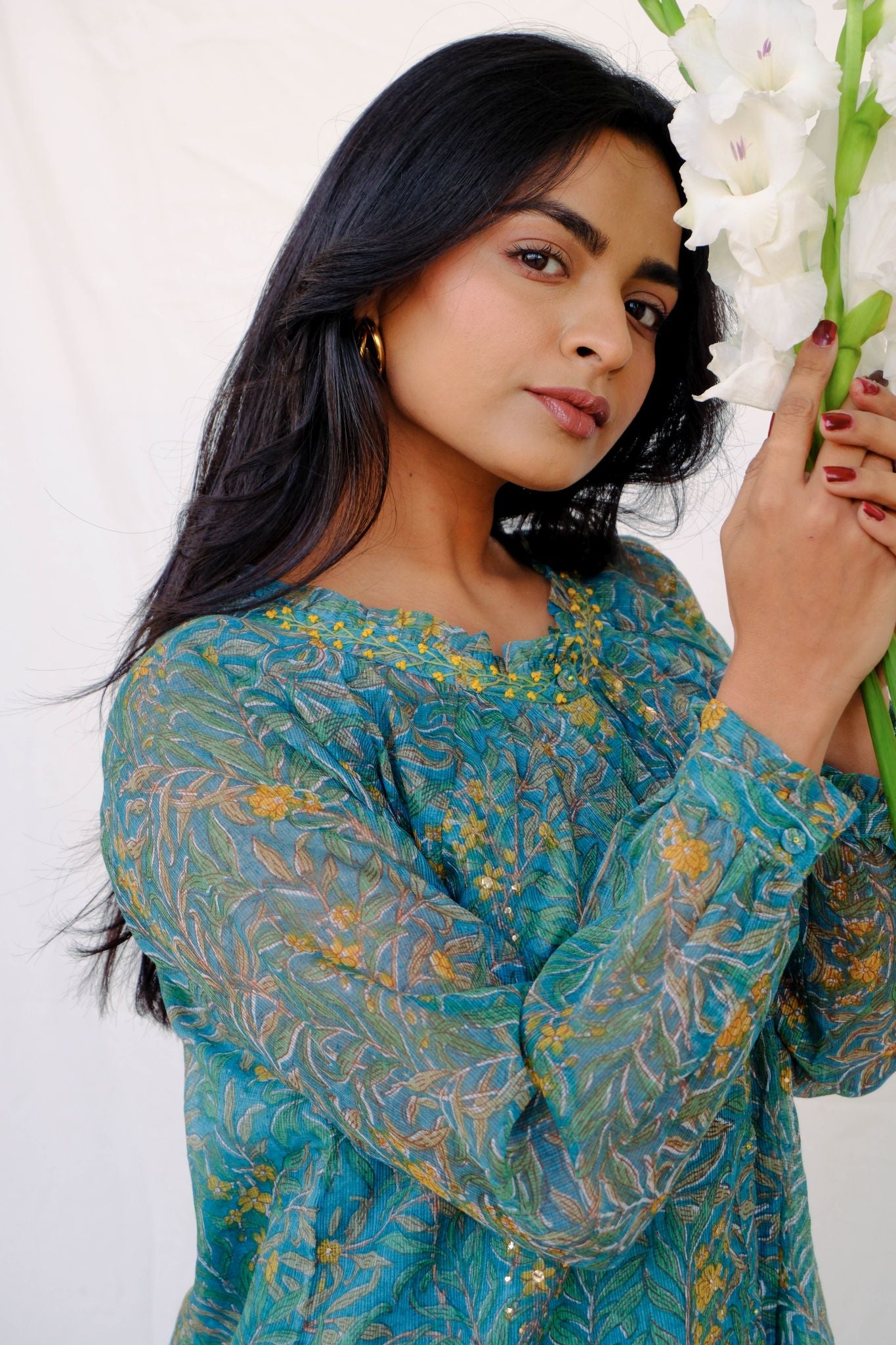 Woman in a blue floral dress holding white flowers against a white background