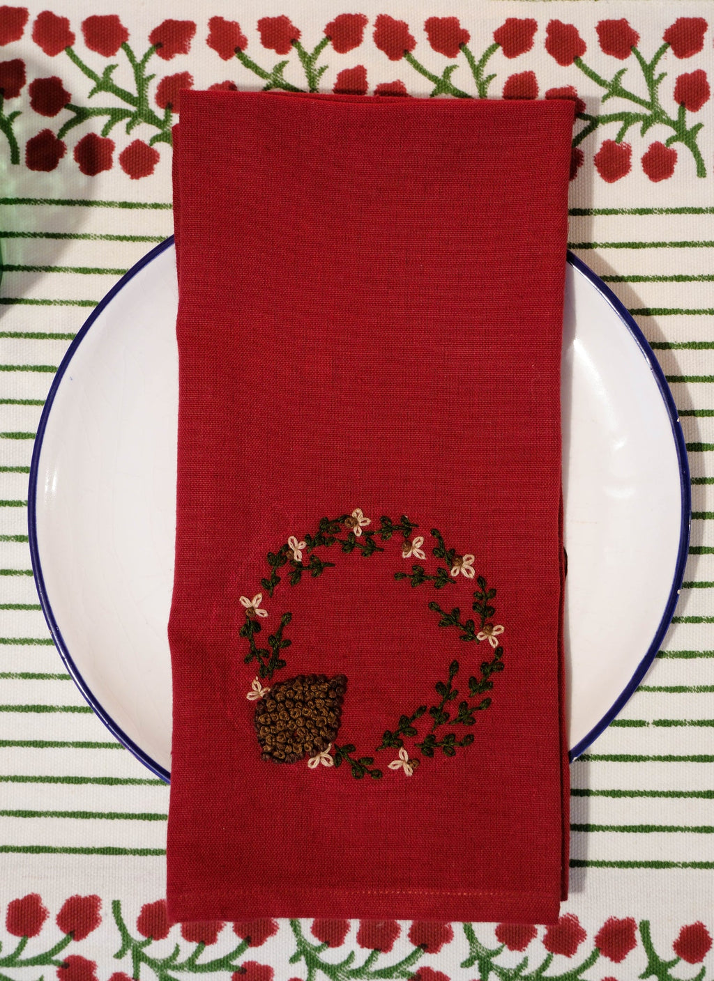 Red napkin with embroidered design on a white plate against a patterned placemat.