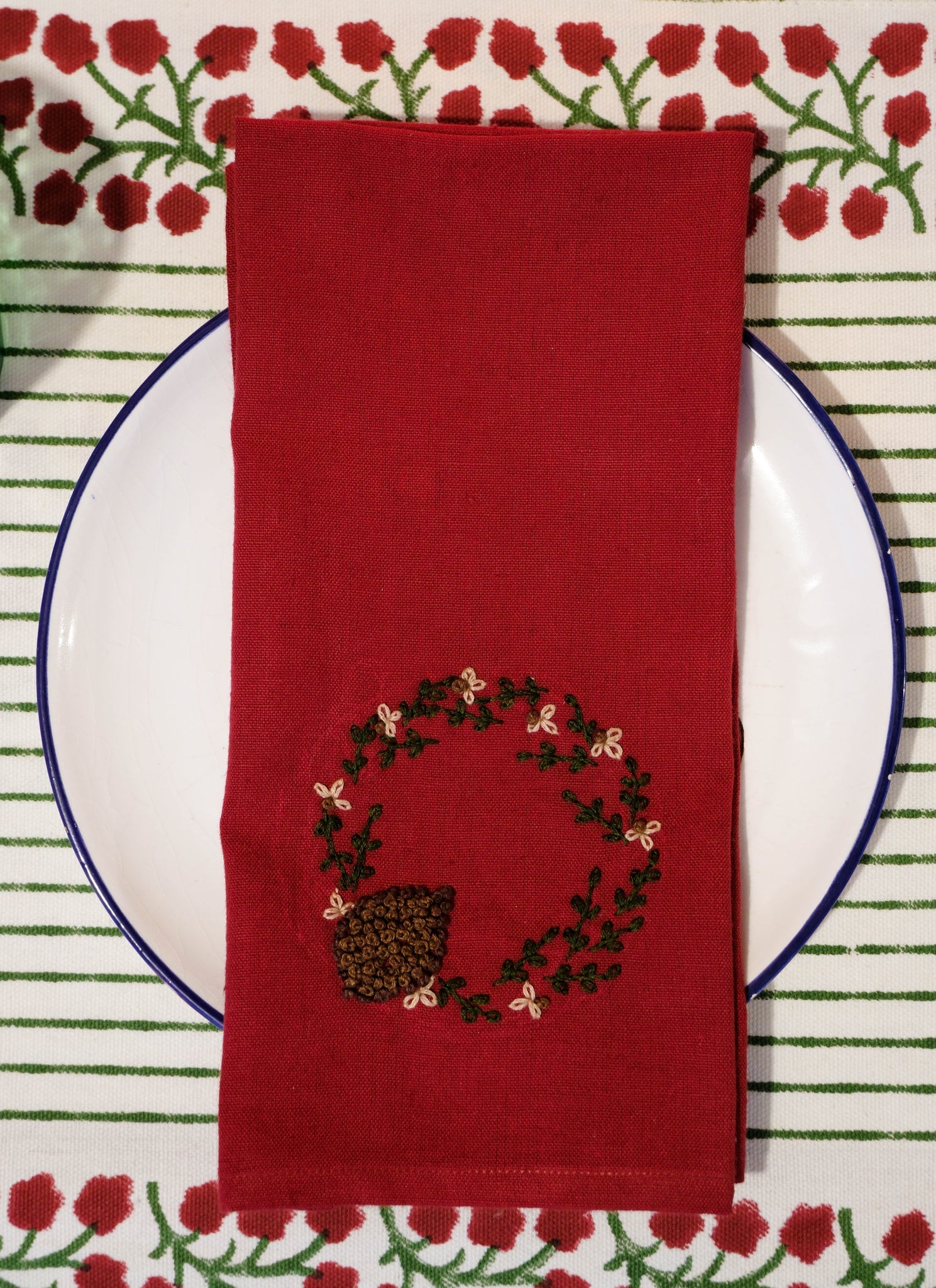 Red napkin with embroidered design on a white plate against a patterned placemat.