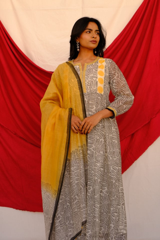 Woman wearing a traditional outfit with a yellow and gray patterned dress against a red and white background
