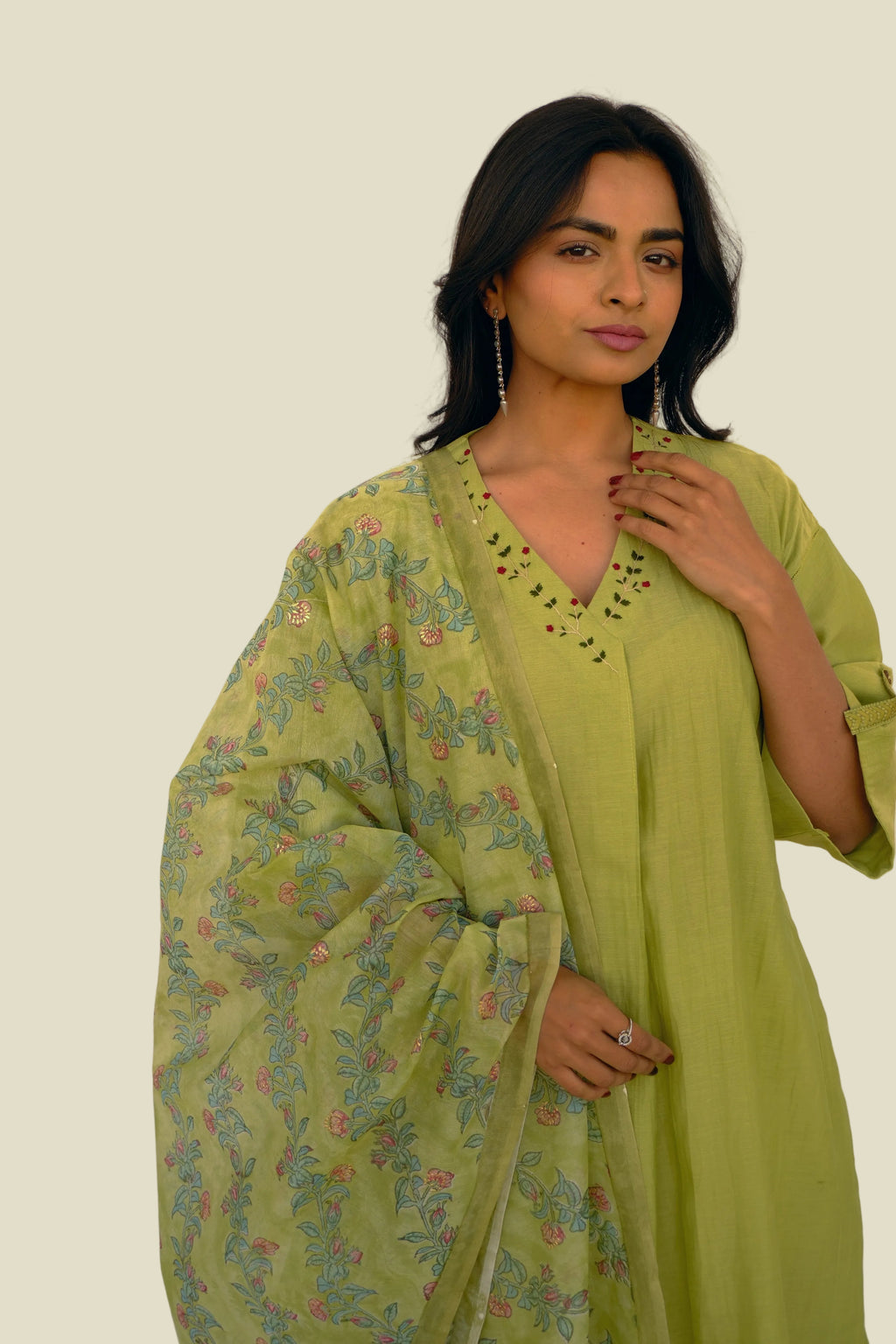 Woman wearing a light green traditional outfit with a floral shawl against a white background