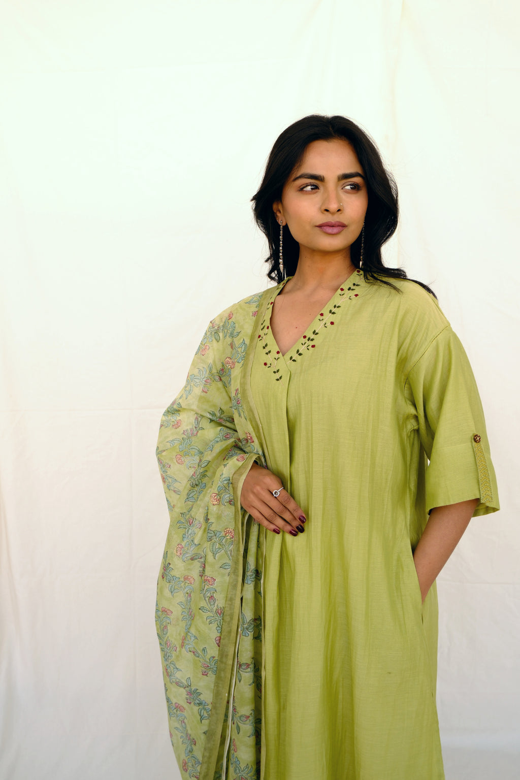 Woman wearing a green dress with floral dupatta against a white background