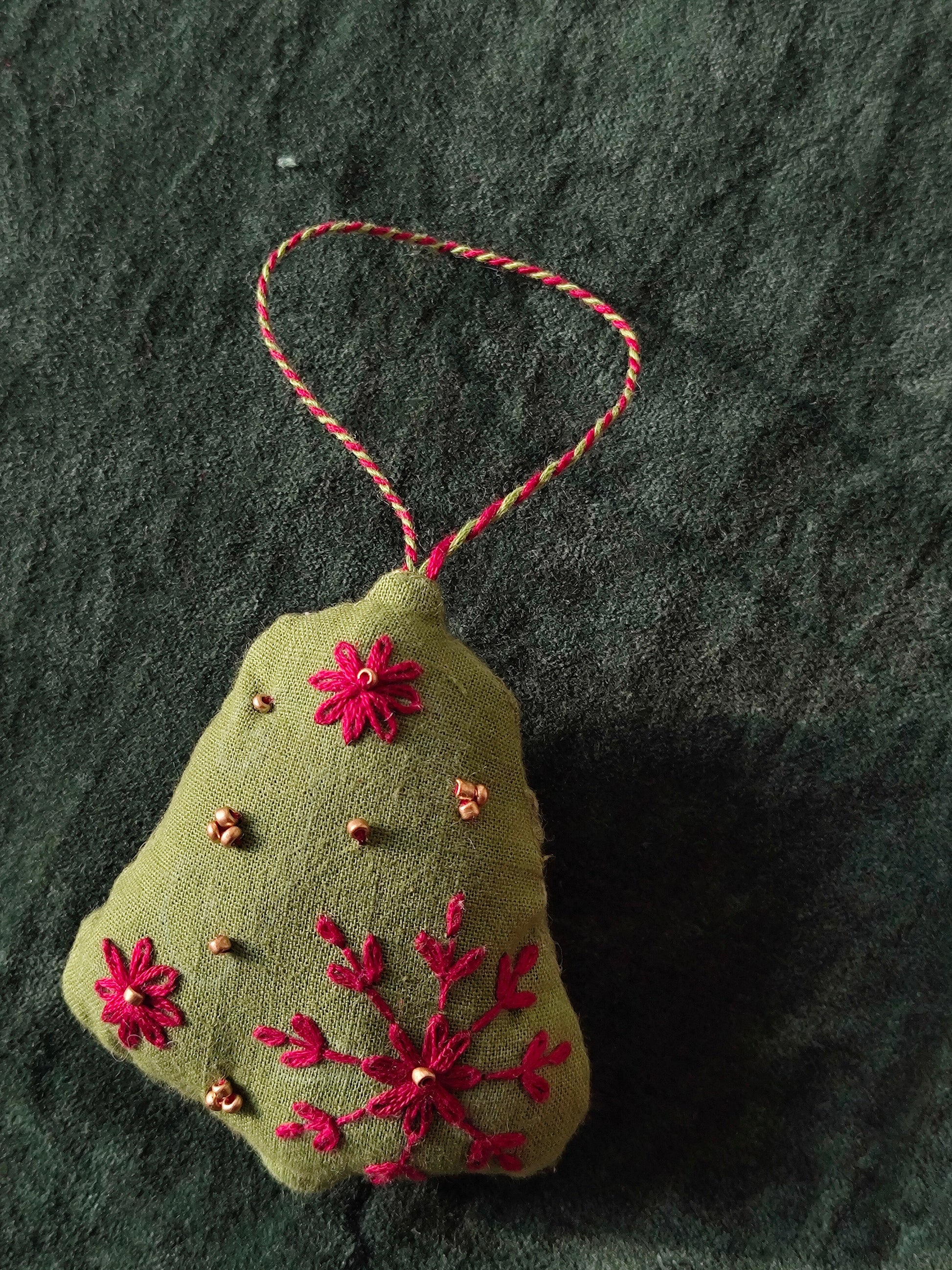 Green fabric ornament with red floral embroidery on a dark textured background
