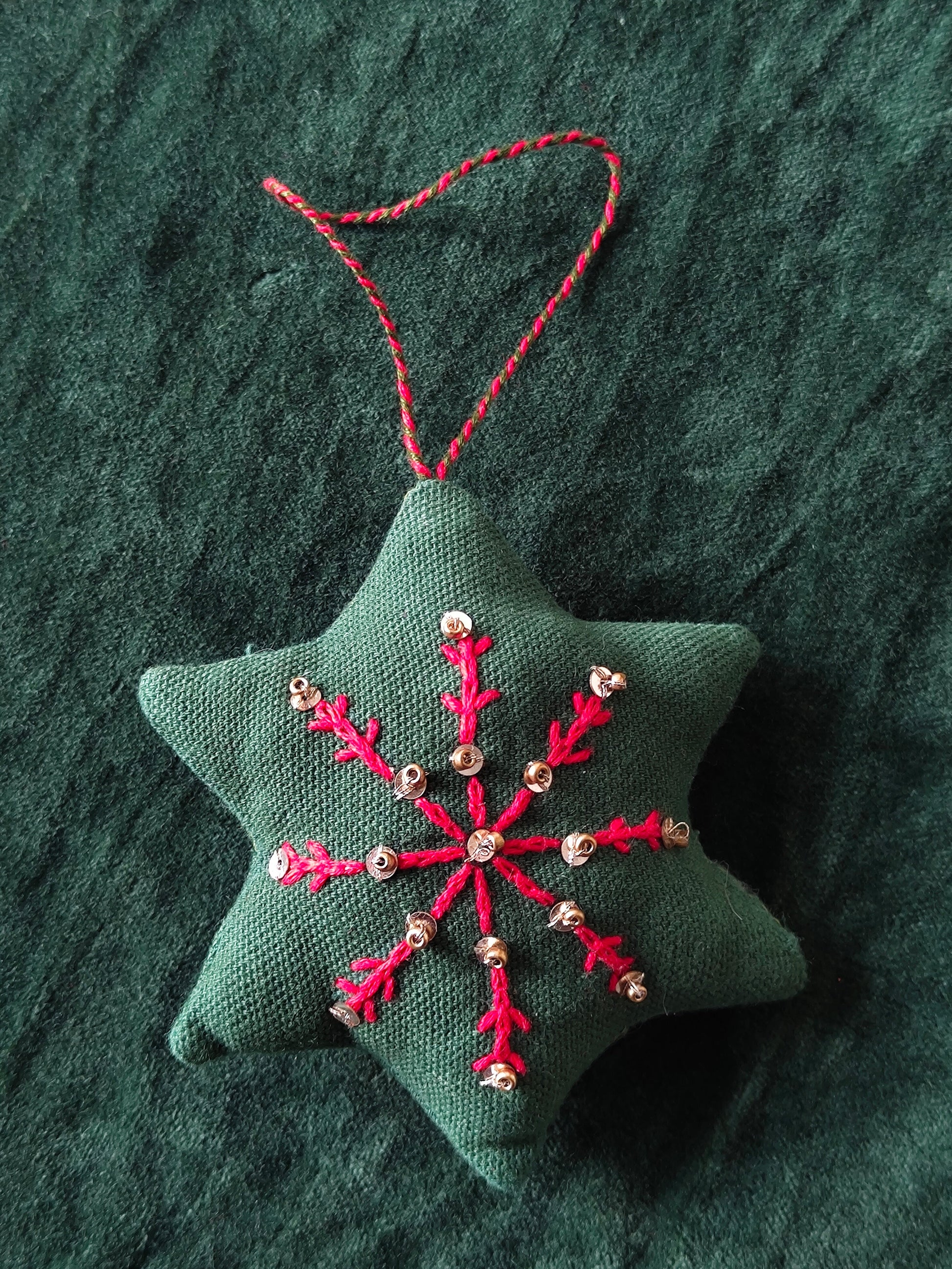 Star-shaped fabric ornament with red embroidery on a textured green background