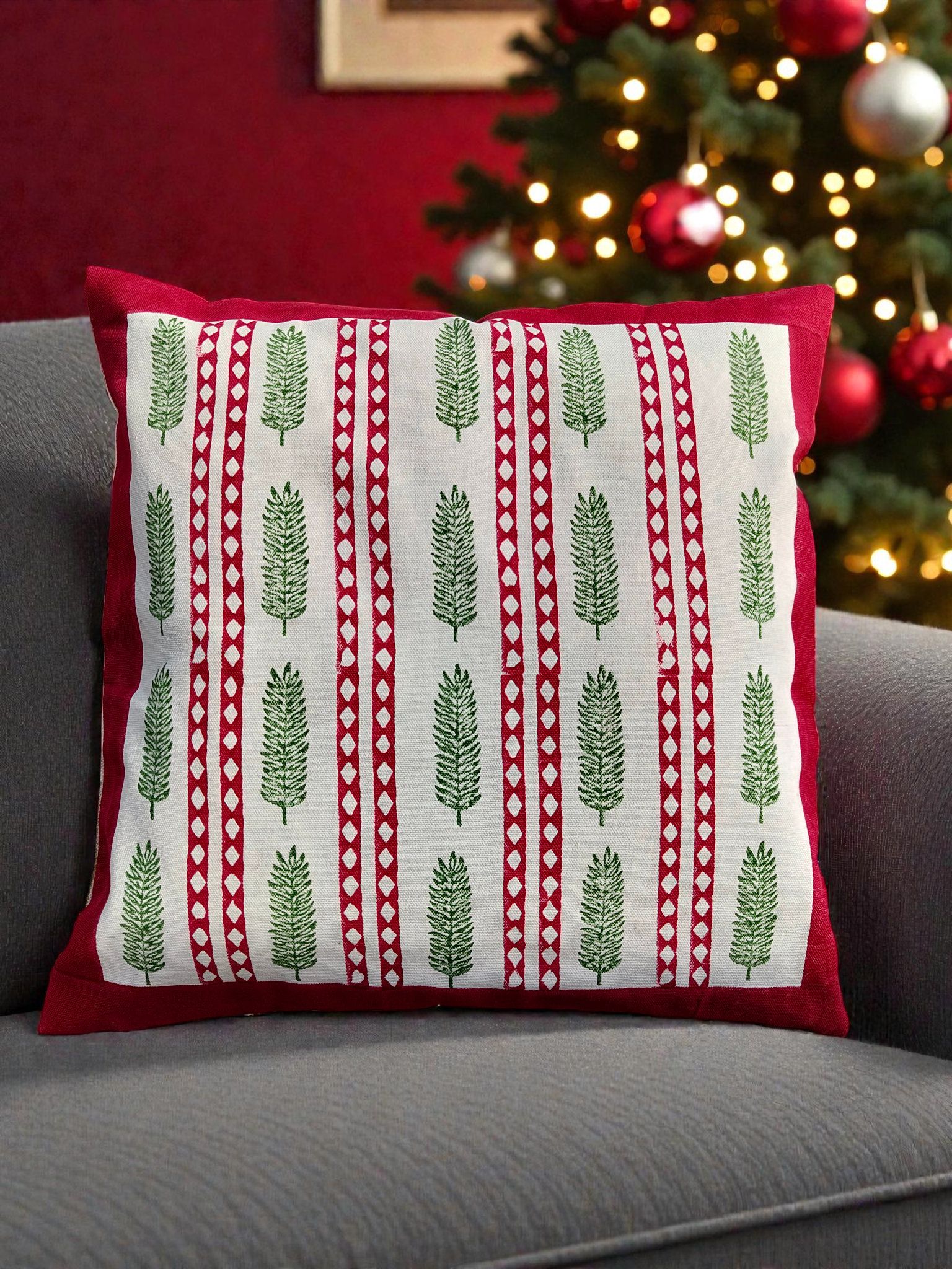 Decorative pillow with green tree pattern on a gray couch with a Christmas tree in the background.