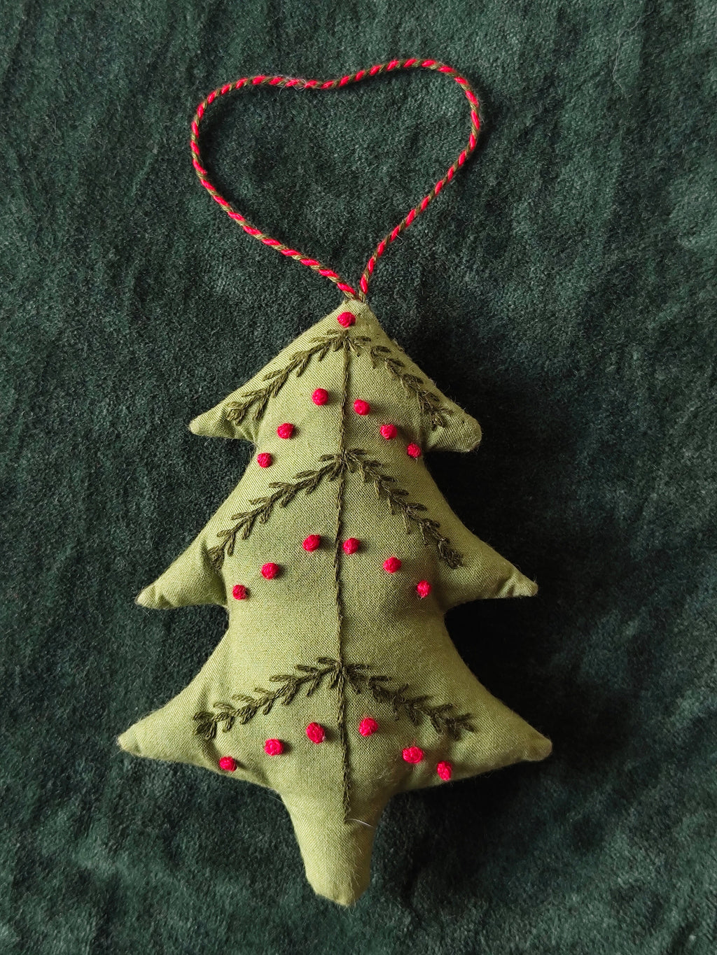 Handmade Christmas tree ornament with red details on a dark fabric background