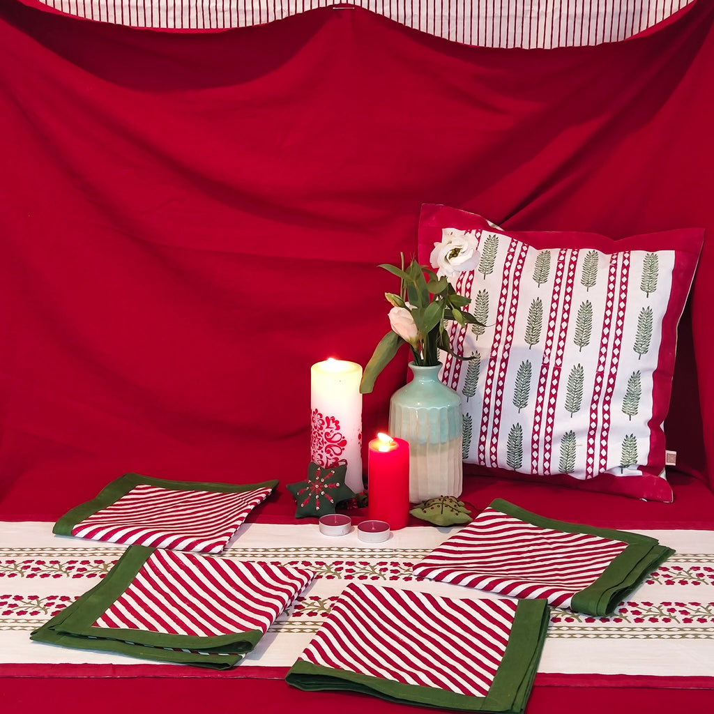 Decorative table setting with red and white floral striped tablecloth, folded napkins,  candles, and a pillow.