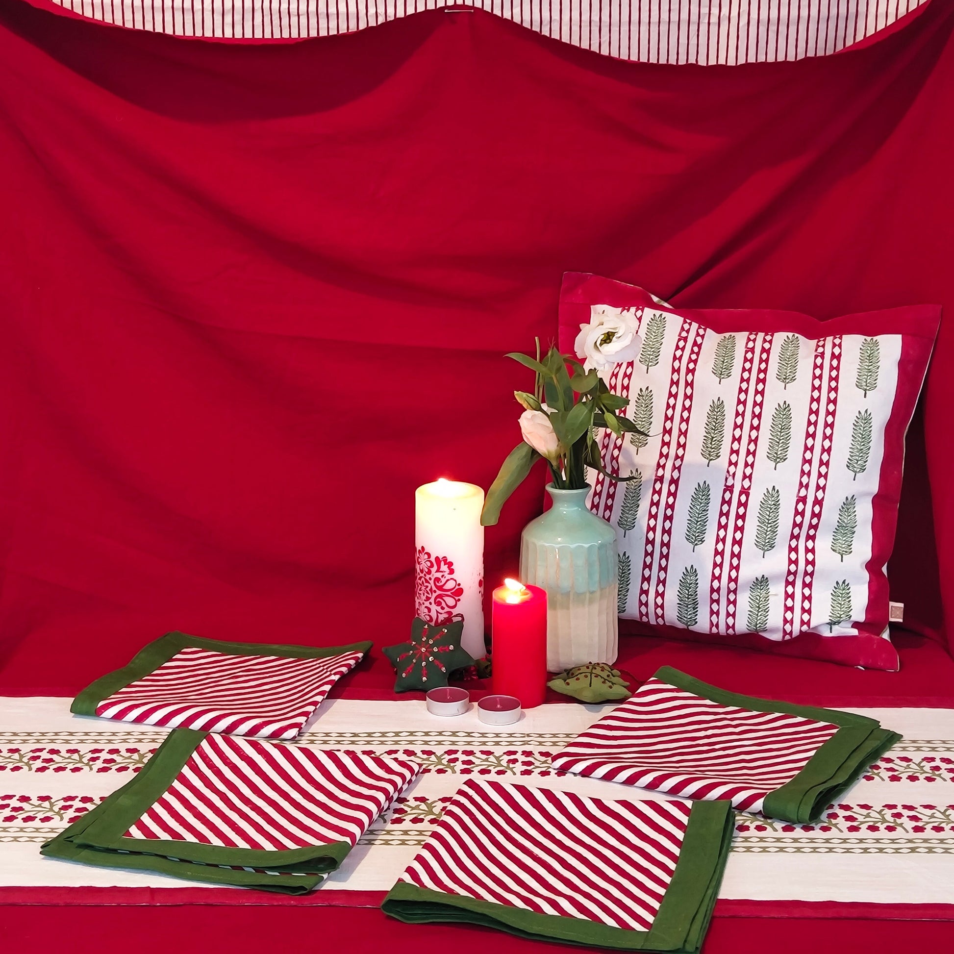 Decorative table setting with red and white floral striped tablecloth, folded napkins,  candles, and a pillow.